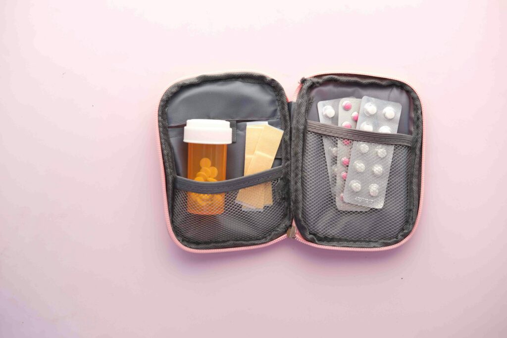 The Lightweight Bikepacking Checklist I’d Actually Recommend Open first aid kit with pill bottle, blister packs, and band-aids on a pastel background.